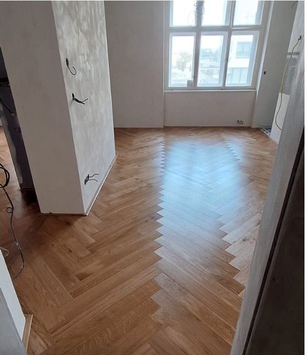 Nová masivní rybinová podlaha v bytě s vysokým oknem